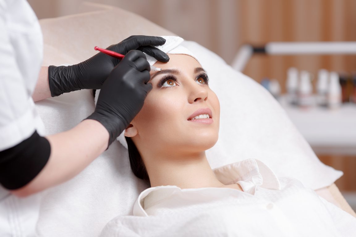 Permanent makeup eyebrows. Mikrobleyding eyebrows workflow in a beauty salon. Cosmetologist applying a special permanent makeup on a woman's eyebrows.